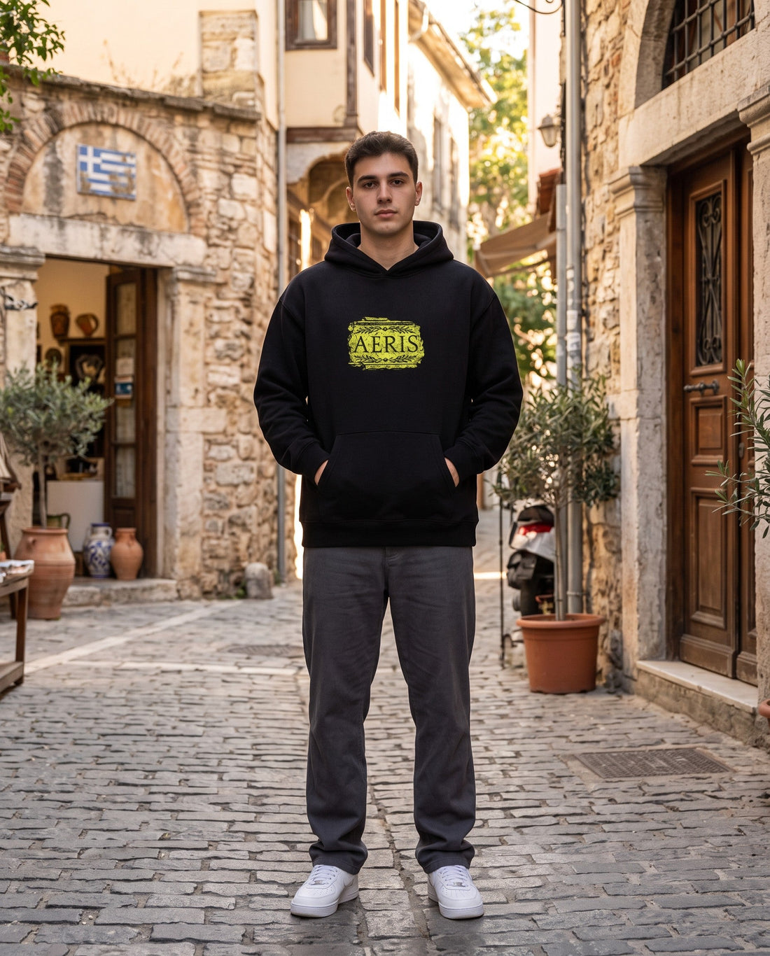 Άντρας σε πέτρινο δρομάκι φορά το oversized AέRis Karyatida hoodie σε μαύρο, με την πέτρινη επιγραφή AέRis στο στήθος