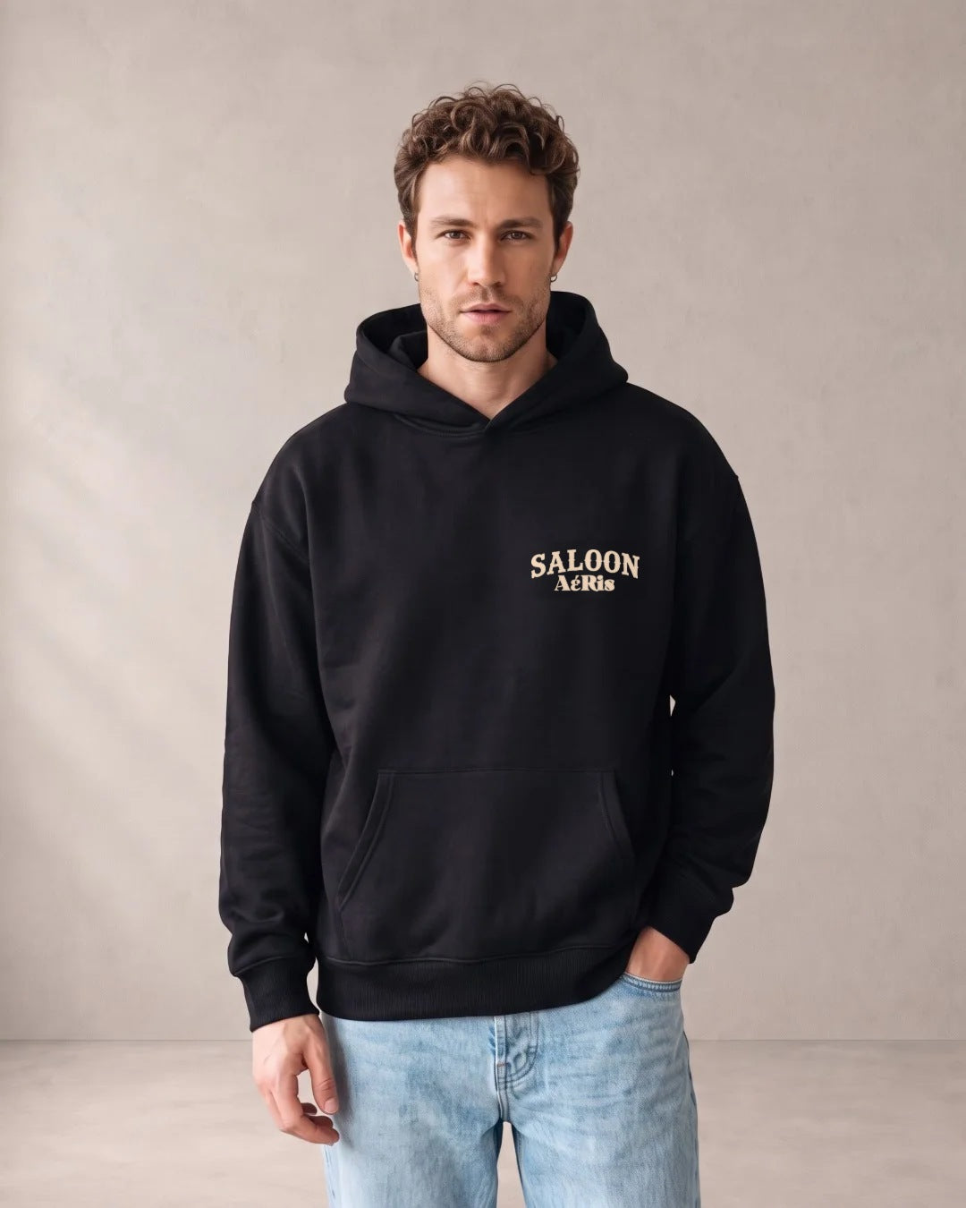 Άντρας φορά το oversized AέRis Saloon hoodie σε μαύρο, με τη στάμπα SALOON στο στήθος