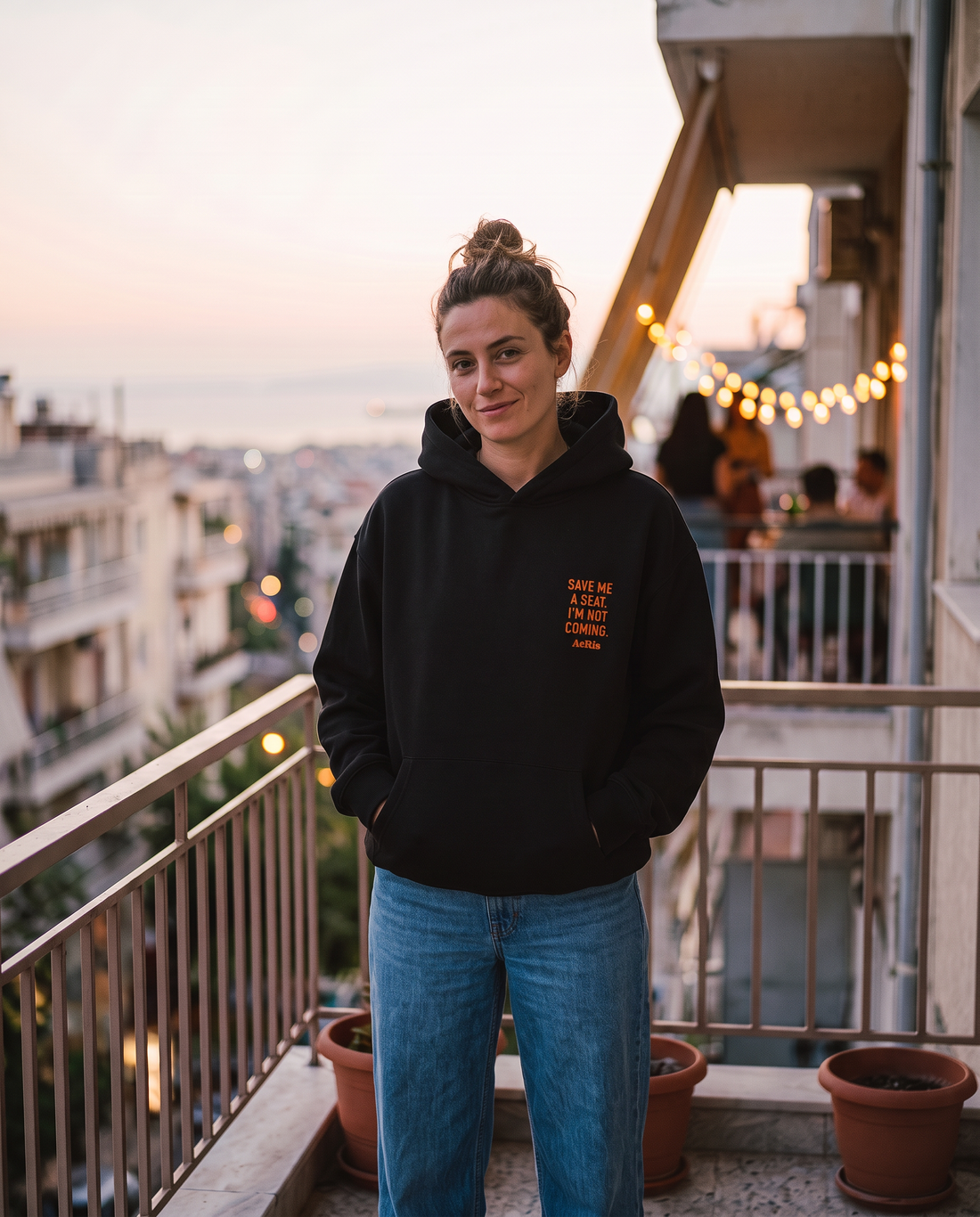 Γυναίκα σε μπαλκόνι στη Θεσσαλονίκη φορά το oversized AέRis Invite hoodie σε μαύρο, με το Save me a seat στην καρδιά